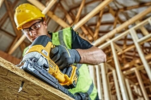 Construction worker in safety gear using a power tool on wood.