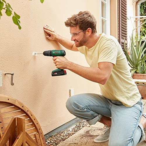 Man using a drill on an outdoor wall.